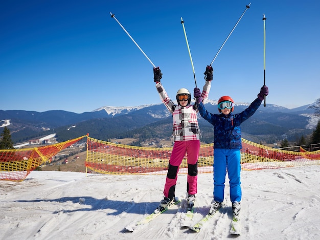 Skier girl and boy on skis on background of winter resort bright blue sky and beautiful mountains