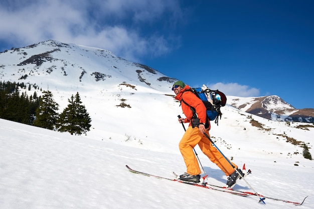 Skier tourist with backpack on background of bright blue sky and beautiful mountain panorama.