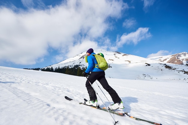 Skier tourist with backpack on background of bright blue sky and beautiful mountain panorama