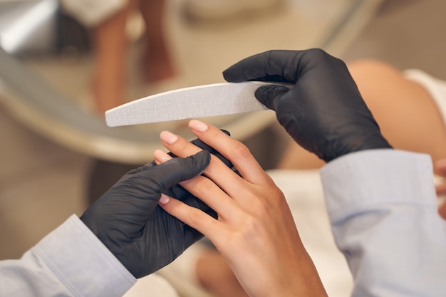 Skilled manicure master using fingernail file while correcting client nail form