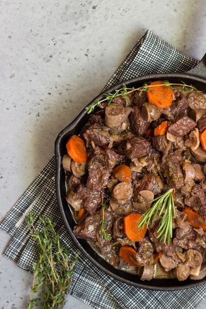 A skillet with beef bourguignon with sausages, carrots, garlic, onion, red wine, herbs and spices.