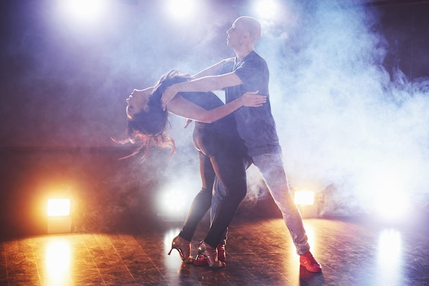 Photo skillful dancers performing in the dark room under the concert light and smoke sensual couple performing an artistic and emotional contemporary dance