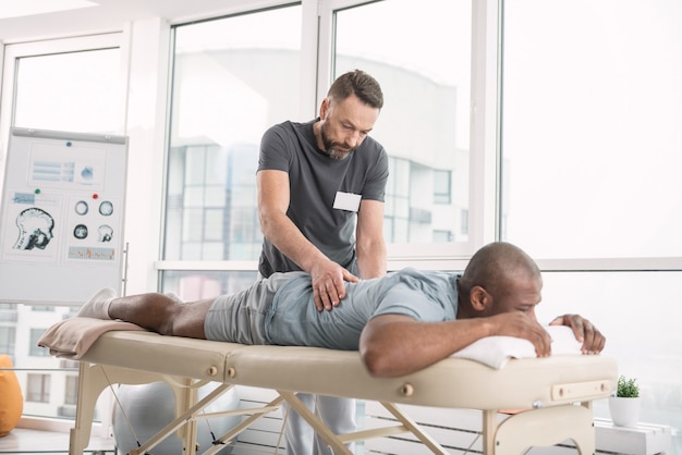 Skillful orthopedist. Skilled bearded man doing a back massage for his patient while working as an orthopedist