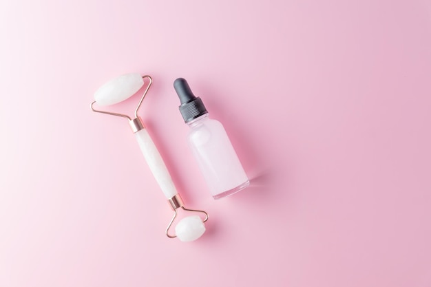 Skin care concept Bottle of cometic product serum or oil Quartz roller Cosmetics and tools on pink background