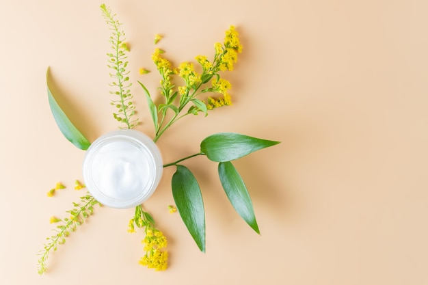 Skin care open cream jar with green leaves and flowers on beige background closeup minimalistic photo for spring product presentation