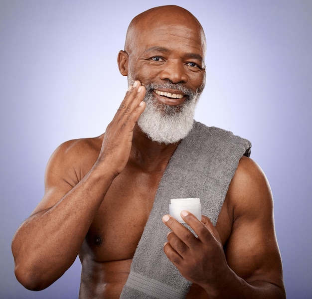 Skincare beauty cream and black man studio portrait with a towel and lotion for cosmetics self care and dermatology product on a purple background Face of black male with a smile for healthy skin