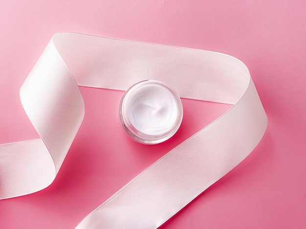 Skincare cosmetics face cream moisturiser jar and white silk ribbon on pink background beauty product flatlay closeup