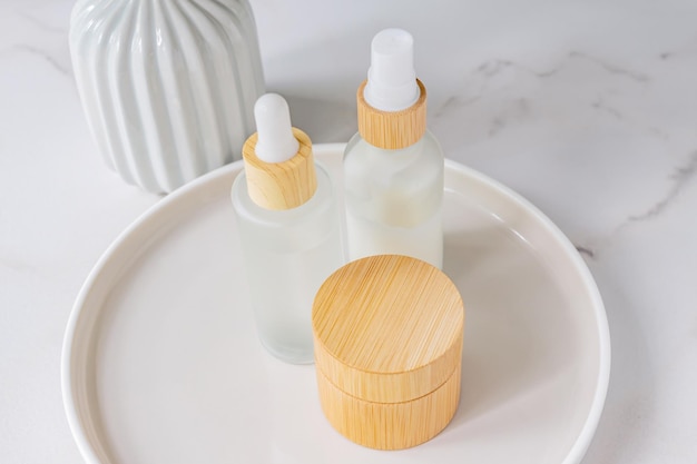 Skincare products set Natural moisturizer cream jar dropper bottle with serum and essence on round ceramic tray on marble background Organic cosmetics concept