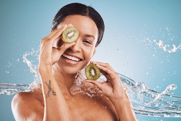 Skincare water and portrait of woman with kiwi for natural organic and healthy beauty products in studio Dermatology wellness and girl with fruit water splash and cosmetics on blue background