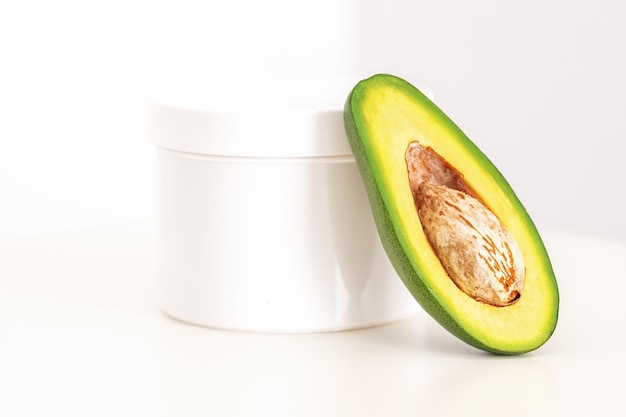 Skincare with natural cosmetics White cosmetic jar of cream with half of the avocado near against white background copy space mockup