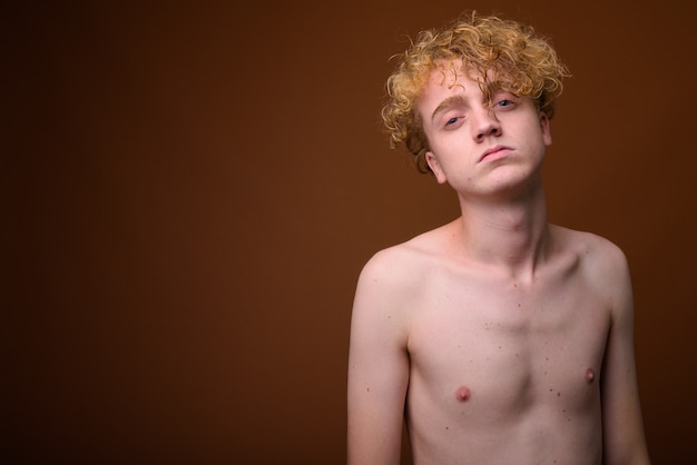 Skinny young man with curly hair shirtless on brown