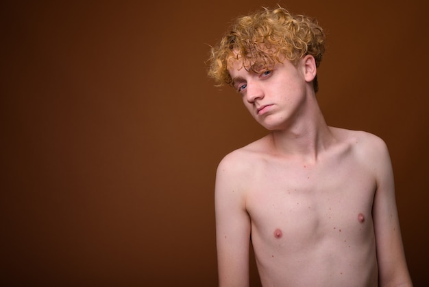 Skinny young man with curly hair shirtless on brown