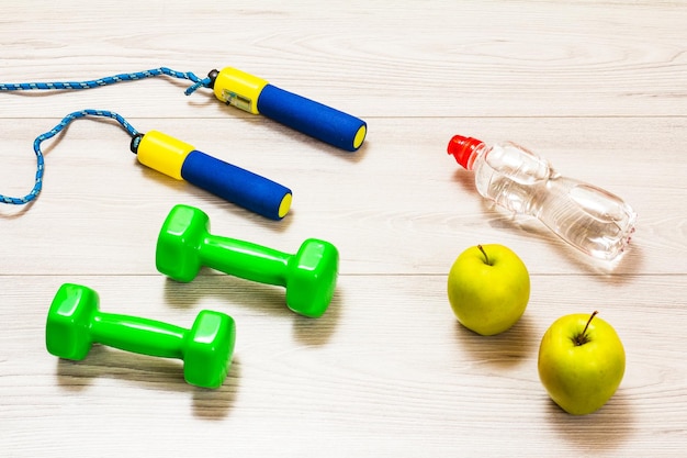 Skipping rop and dumbbells for fitness, a bottle of water and apples in a room or a gym on the gray floor. Top view.