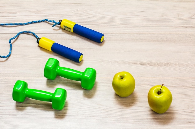 Skipping rope and dumbbells for fitness and apples in a room or a gym on the gray floor Top view