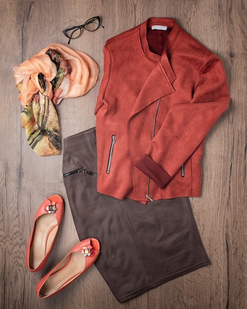 Skirt, jacket, scarf, shoes and glasses outfit flat lay on wooden background