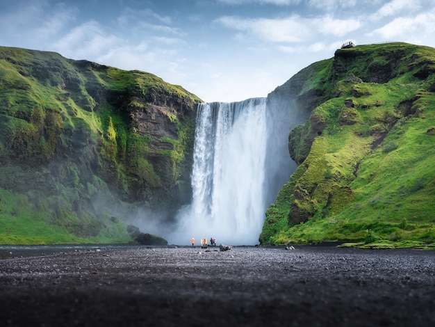 Skogafoss waterfall Iceland Mountain valley and clear sky Natural landscape in summer season Icelandic nature Group of a people near large waterfall Travel image