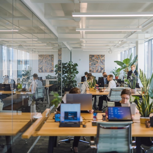 A sleek openplan office with glass walls ergonomic furniture and natural light Professionals collaborating with laptops and tablets