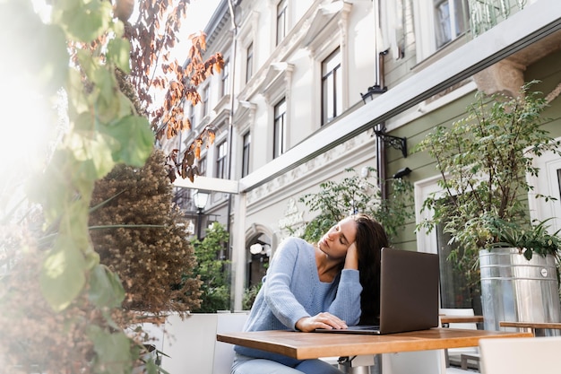 Sleeping girl with laptop on the table outdoor in cafe Tired young woman have a break at work and sleeping and relaxing at laptop on workplace due to overtime work