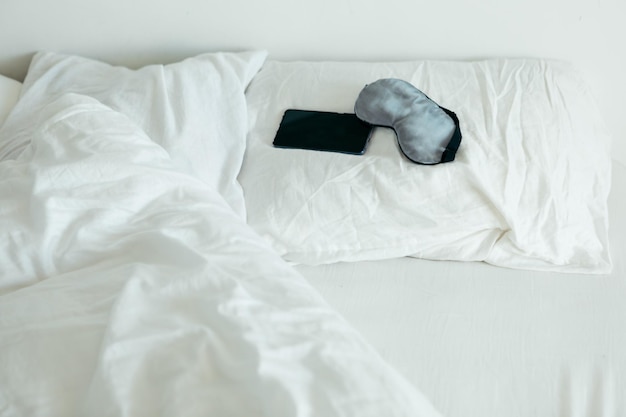 Sleeping mask with phone at bed with white sheets sunny morning