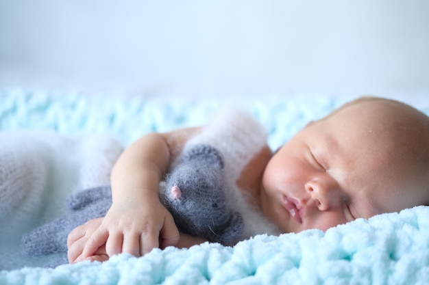 A sleeping newborn baby lies on a blue blanket, a crocheted toy mouse in the baby's hands