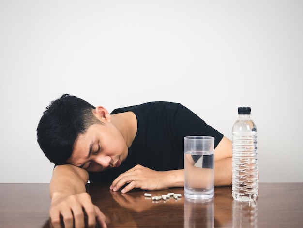 Sleepless man laying at table with medicine pill and water feels sick