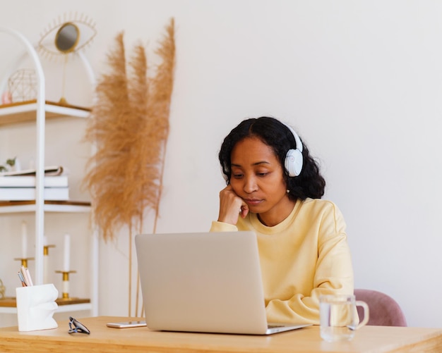 Sleepy africanamerican female student in headphones attending online lecture on laptop at home