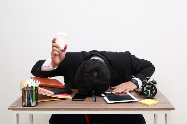 Photo sleepy bored man office worker lying on table with laptop holding and showing paper coffee cup feeling lack of energy sitting at workplace indoor studio shot isolated on white background