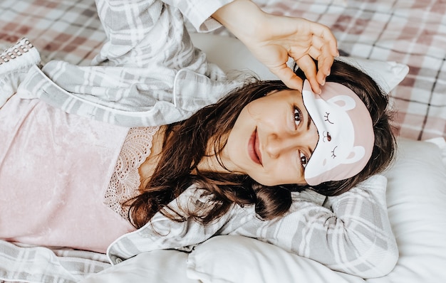 A sleepy brunette girl lies in bed with a blindfold waking up in the morning