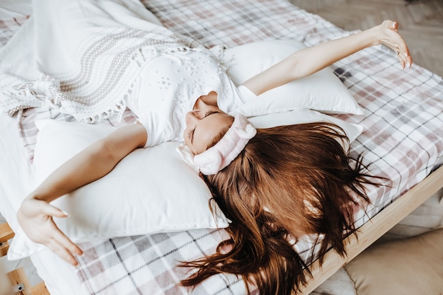 A sleepy brunette girl lies in bed with a blindfold waking up in the morning