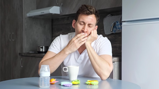 Sleepy father naps and drinks cup of coffee in kitchen