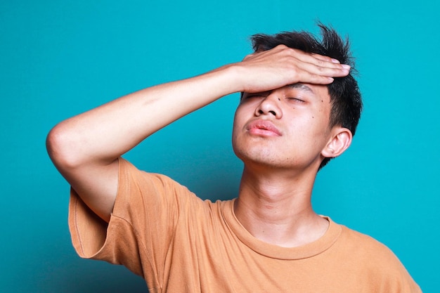 Sleepy and Tired Young Man Touching Forehead Feeling Bored and Lazy Isolated on Blue Background