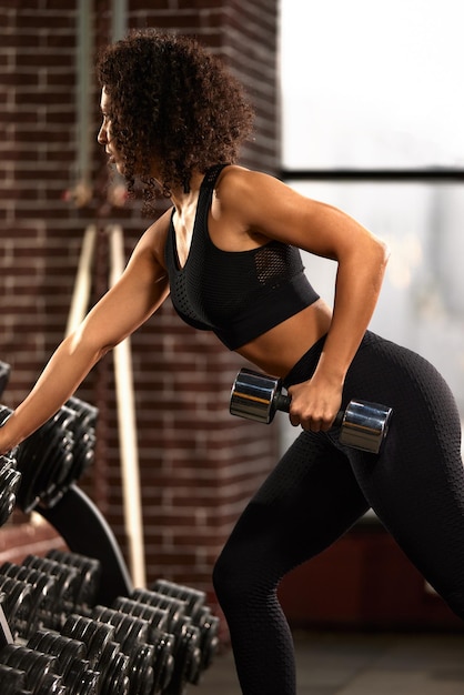 A slender athletic african american woman in sportswear does exercises with dumbbells in the gym