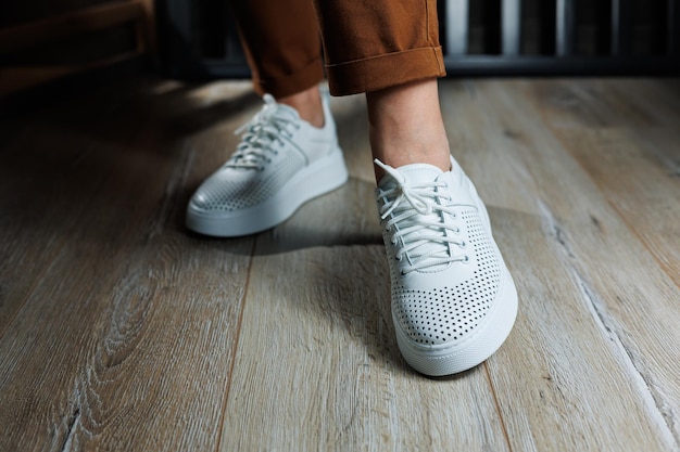 Slender female legs in pants closeup in white casual sneakers Women's leather shoes