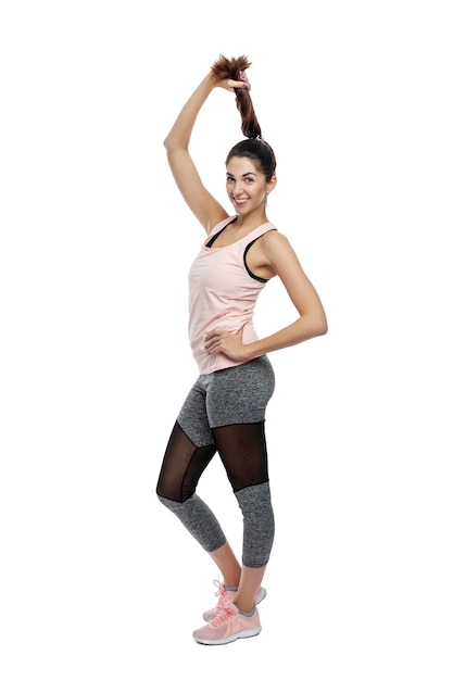 Slender smiling woman in sportswear A beautiful brunette holds her braid in black leggings and a pink top Activity energy and sport Isolated on a white background Full height Vertical