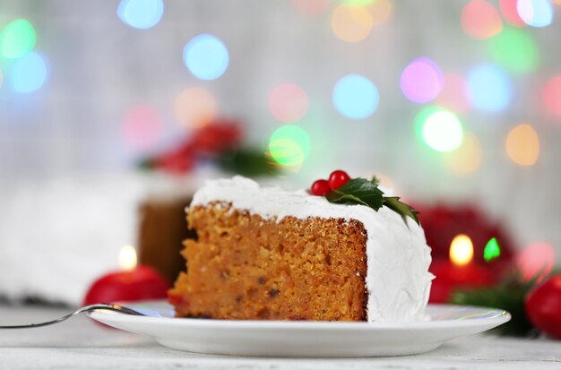 Slice of cake covered cream with Christmas decoration on table, on bright background