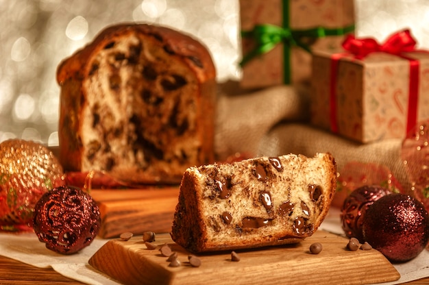 Slice of chocolate panettone  on wooden cutting board with christmas ornaments