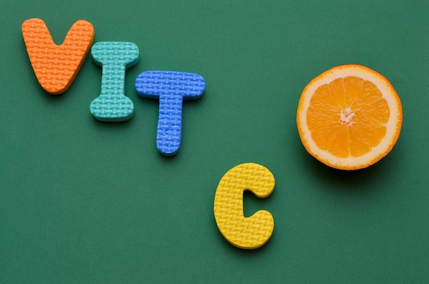 A slice of fresh orange and letters inscription vitamin C on a green background