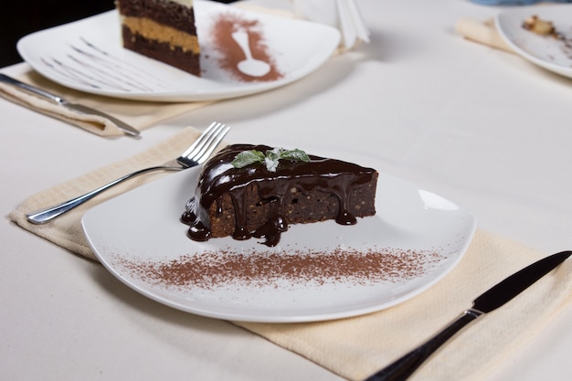 Slice of freshly baked chocolate dessert for dinner topping with rich cocoa icing served on a plate at a restaurant table