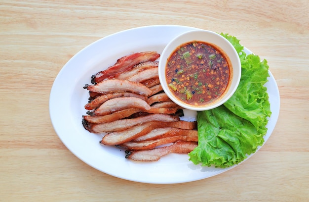 Slice grilled pork served with spicy sauce on white plate on wood table background thai style food