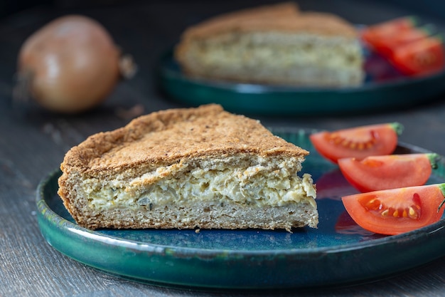 Slice of homemade onion quiche a baked cream and egg pie topped with cheese and green herbs, close up