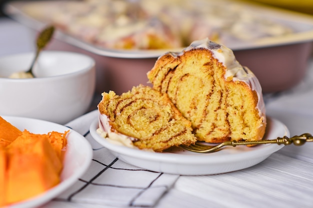 Slice of Homemade Pumpkin cinnamon rolls with cream cheese in a baking dish, close up, selective focus. Seasonal autumn homemade pastry - cinnabons for breakfast or holidays.