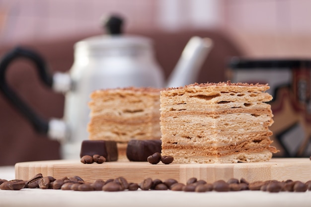 Slice of layered honey cake with coffee beans, candies and black cup, selective focus