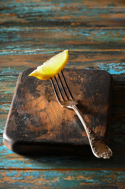 Slice lemon on antique fork on burnedout kitchen board on rough wooden table