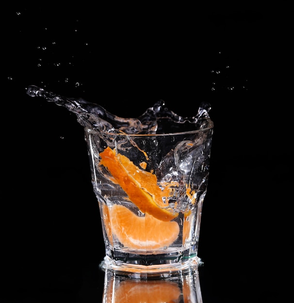 Slice of lemon splashing into a glass of water with a spray of water droplets in motion suspended in the air above the glass on a dark background.