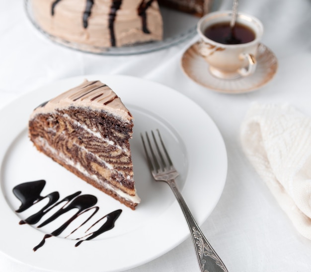 A slice of marble cake with cream Garnished with icing and chocolate On a white plate with a fork Closeup