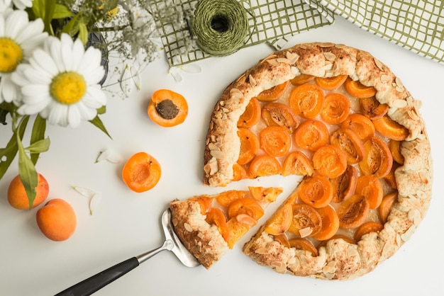 A slice of peach tart with a fork on a table with flowers behind it.