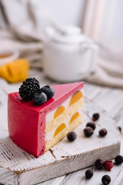 A slice of a pink strawberry cheesecake served with fresh berries on a white board