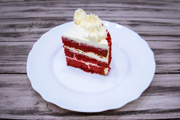 Slice of red velvet cake with cream on a white plate on a gray background