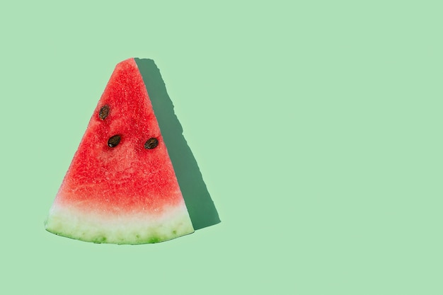 Slice of ripe watermelon on mint green background with copy space.