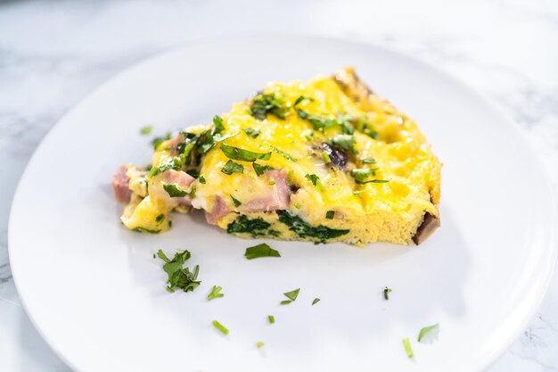 Slice of spinach and ham frittata on a white dinner plate